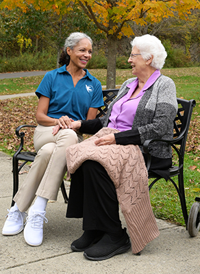 A Visiting Angels caregiver comforting an elderly woman on a park bench.