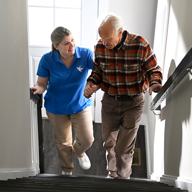 A female Visiting Angels caregiver helps an elderly man walk up the steps.